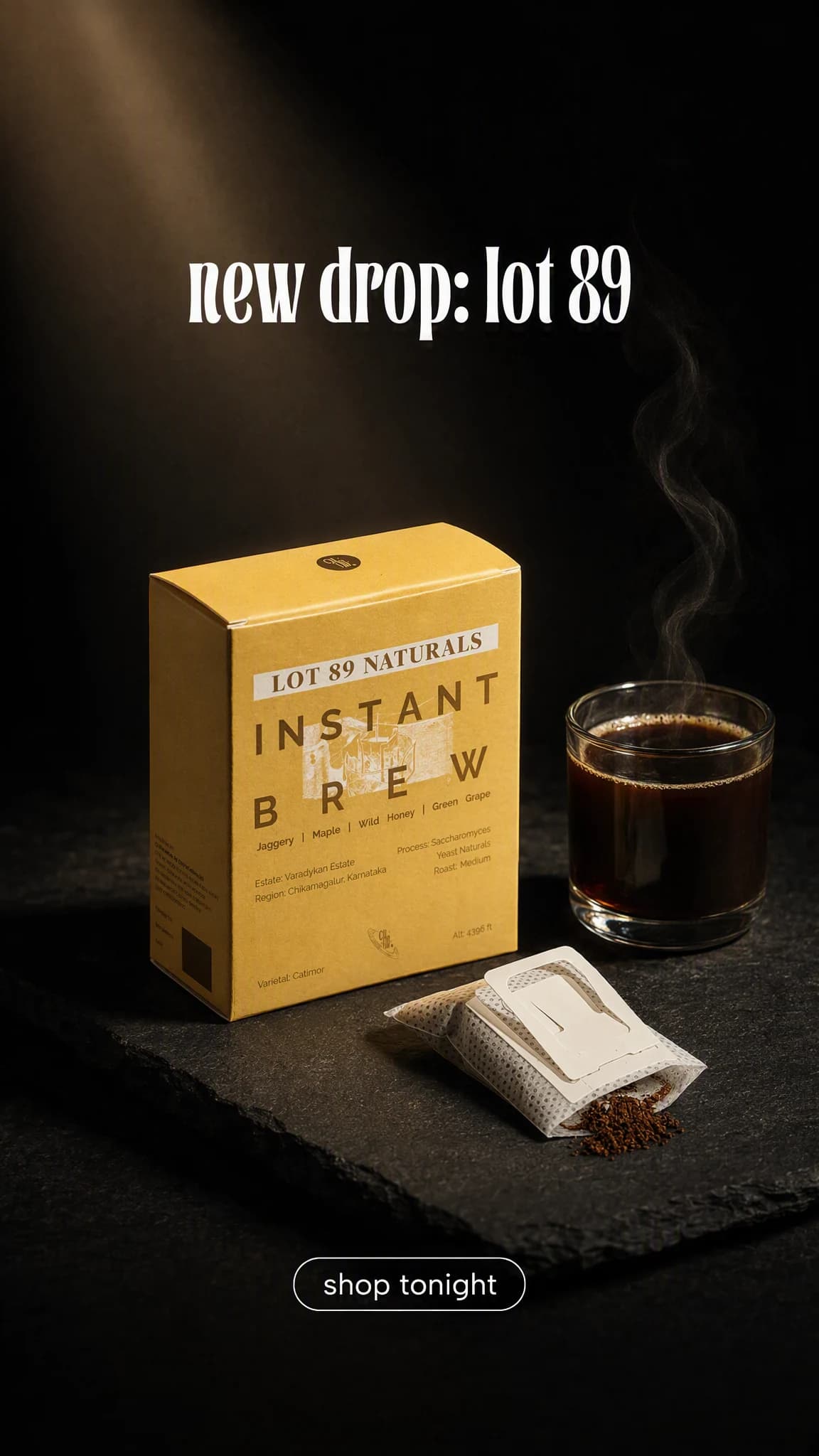 A single dramatic frame: the coffee pack and sachet lit under a warm spotlight beside a steaming cup on a dark surface.