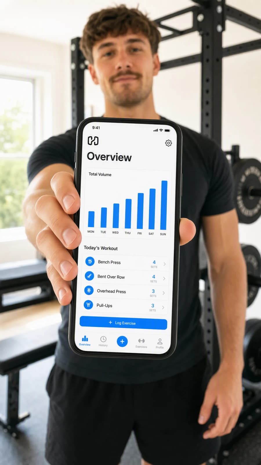 A lifter holding up a phone showing a workout-tracking app with a weekly volume chart and a list of today's exercises, fully readable against a gym backdrop.