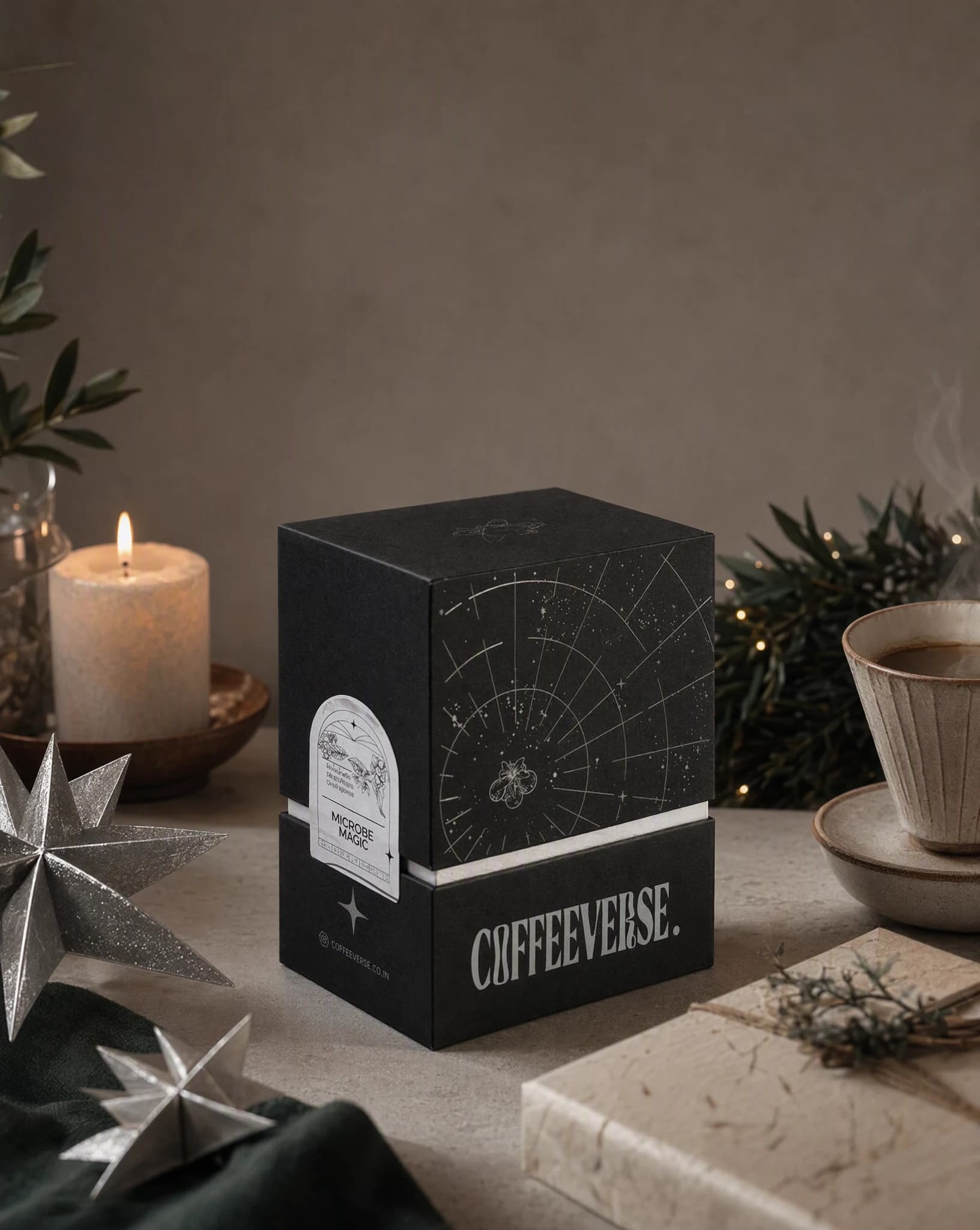 A Coffeeverse coffee box restaged in a restrained winter gifting scene with stars, ribbon, and candlelight.