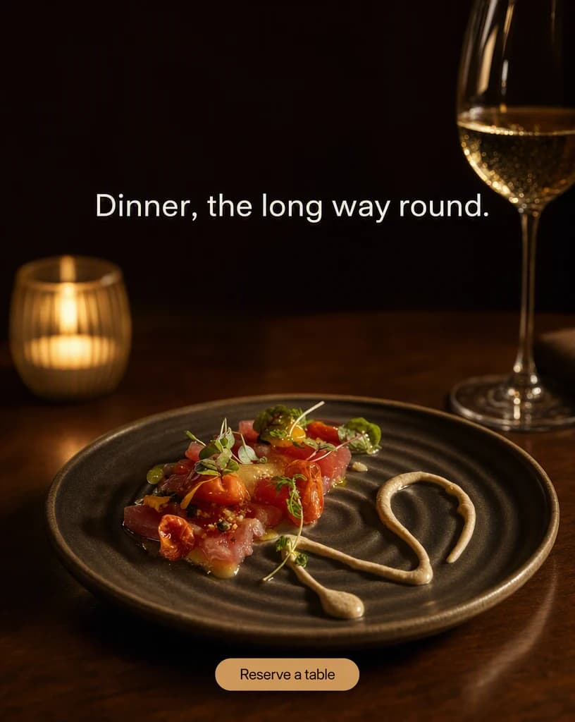 A plated dish on a dark ceramic plate at a restaurant table in warm low light with a candle out of focus behind and a wine glass catching a highlight, the upper third dark and clear.