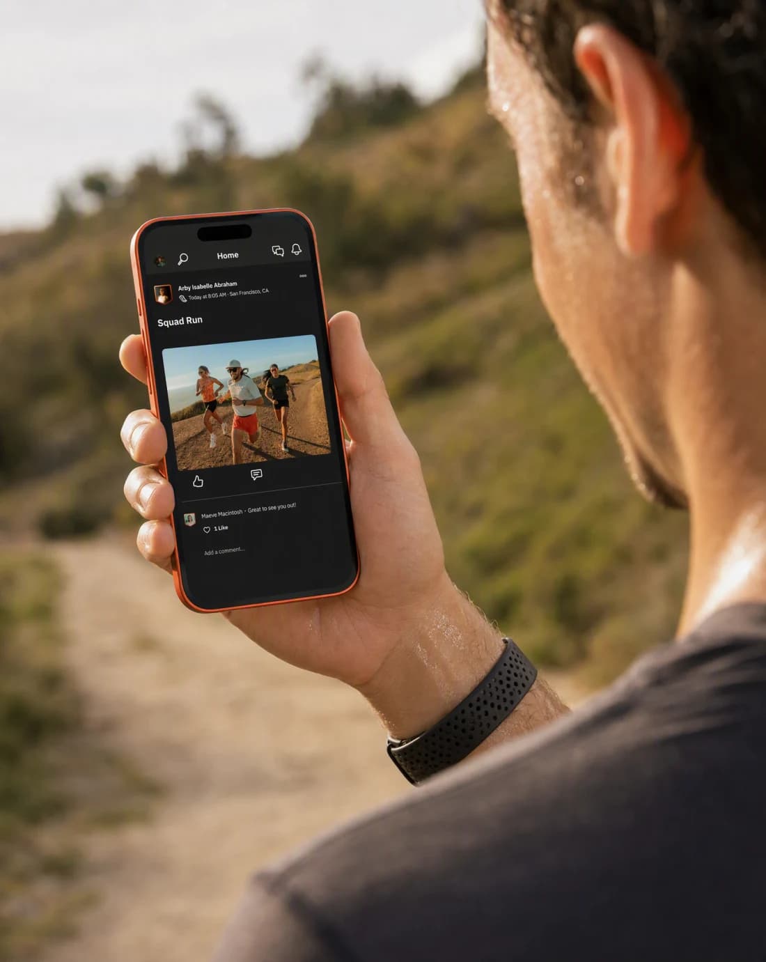A runner outdoors holding up a phone displaying the Strava app feed with a shared run post, morning light on a trail.