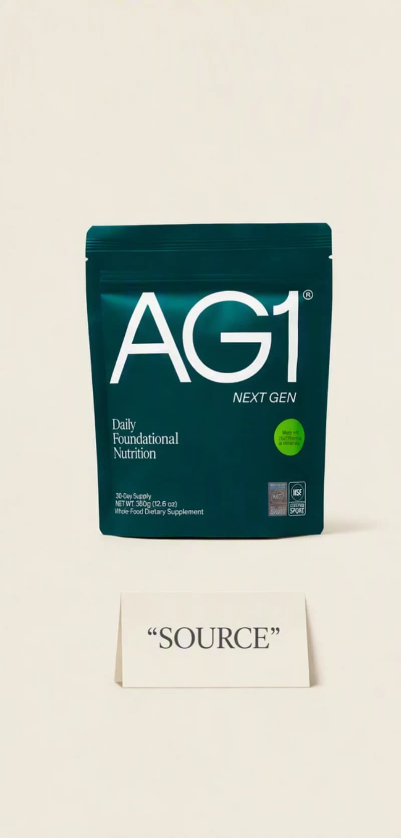 A real AG1 Next Gen pouch centered on a plain cream surface, with a small card reading source placed beneath it.