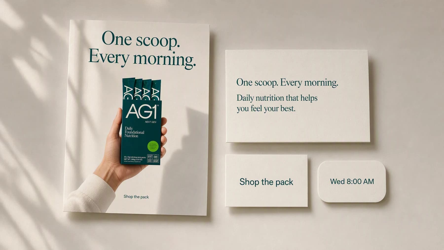 A finished feed post laid out as printed cards on a warm neutral surface: a poster of a hand holding a green supplement stick pack box headlined “One scoop. Every morning.”, beside a caption card, a “Shop the pack” card, and a “Wed 8:00 AM” time chip.
